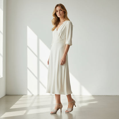 Woman wearing a white dress standing in a bright room with sunlight streaming through the window.