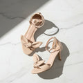 Pair of beige high-heeled sandals with bow details on a white surface
