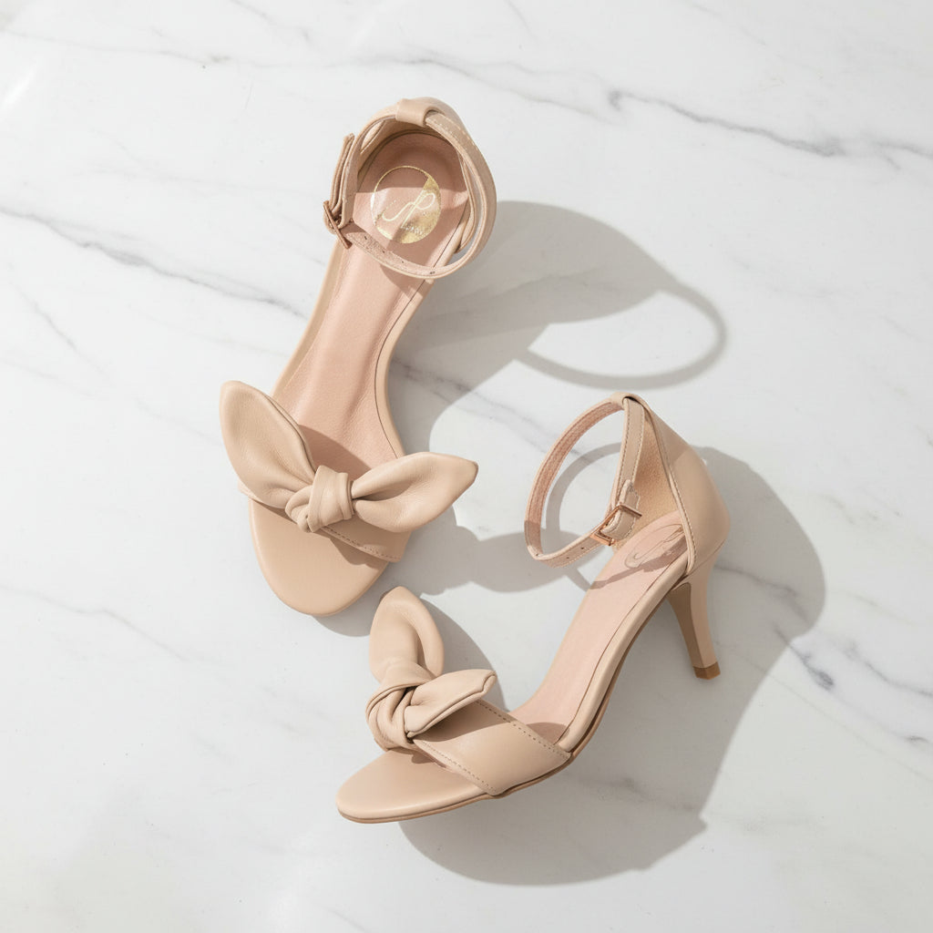 Pair of beige high-heeled sandals with bow details on a white surface