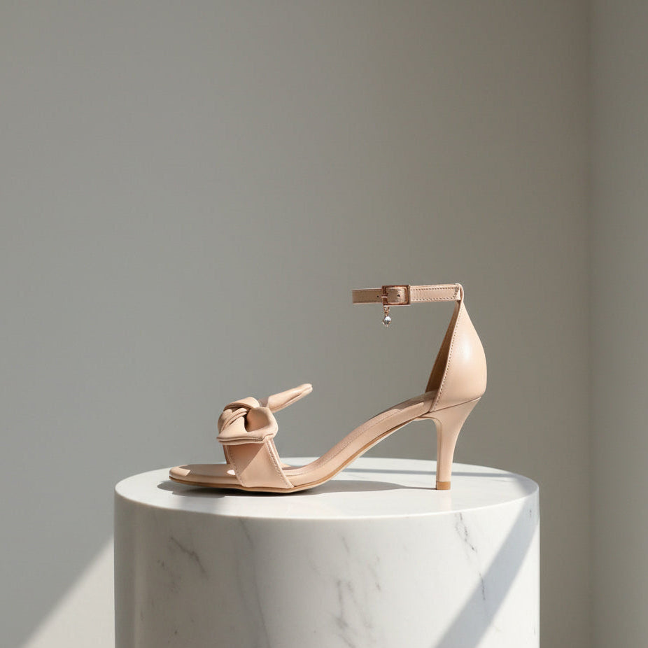 Beige high-heeled sandal on a white marble pedestal with a gray background