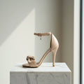 Beige high-heeled sandal on a marble surface with a neutral background