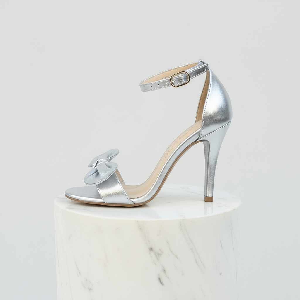 Silver high-heeled shoe with a bow on a white marble pedestal