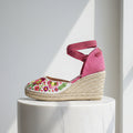 Pink wedge sandal with floral embroidery on a white pedestal against a light gray background