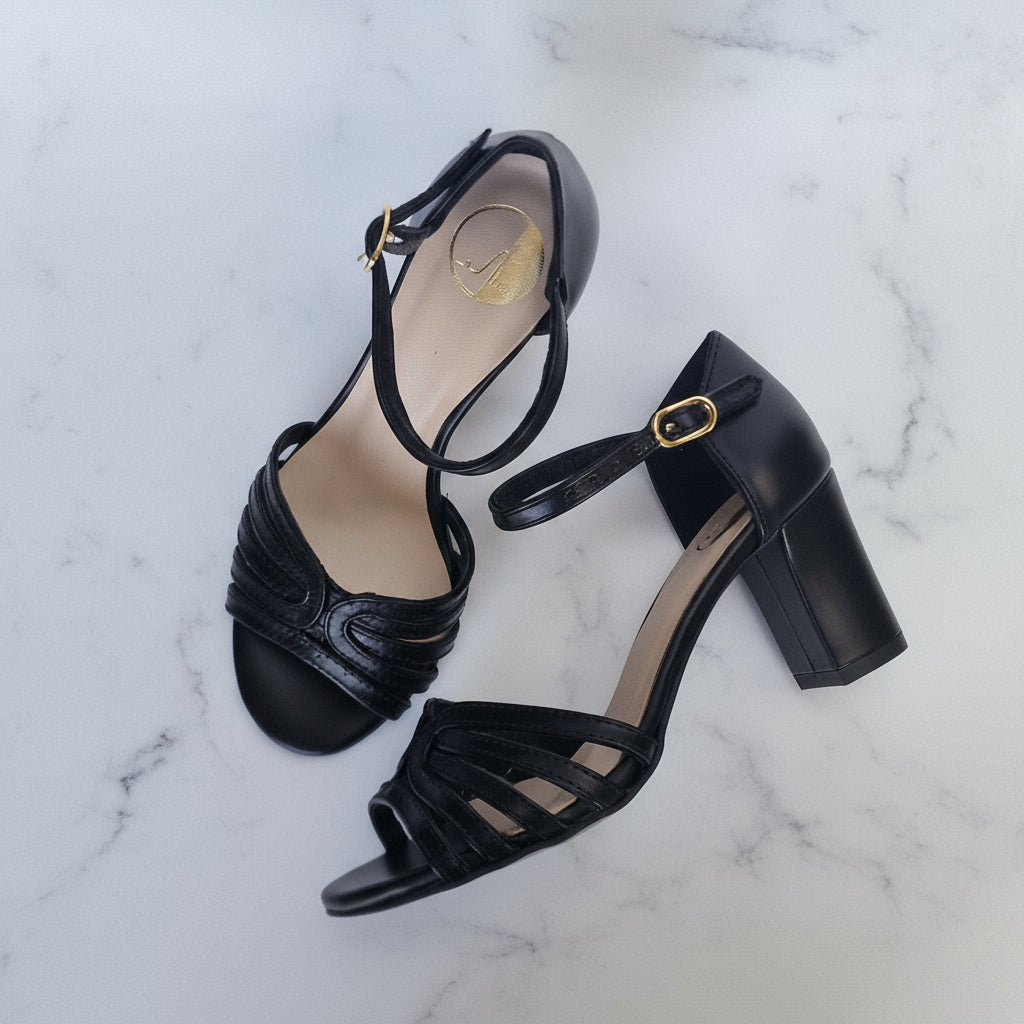Black high-heeled sandals with gold straps on a marble background