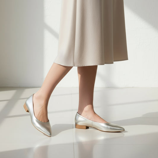 Silver pointed-toe flats worn with a beige skirt on a light background