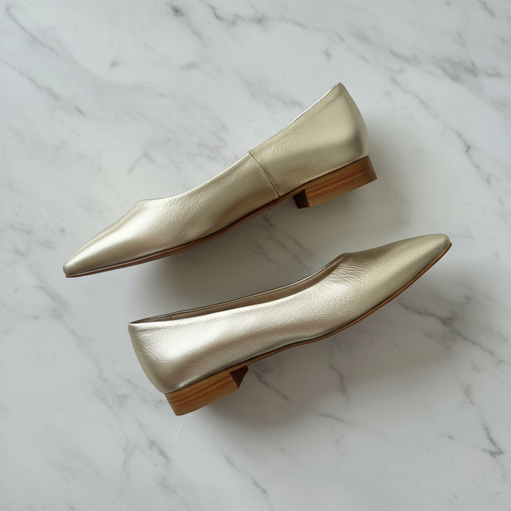 Side view of petite small size gold leather pointed toe ballerinas on marble surface