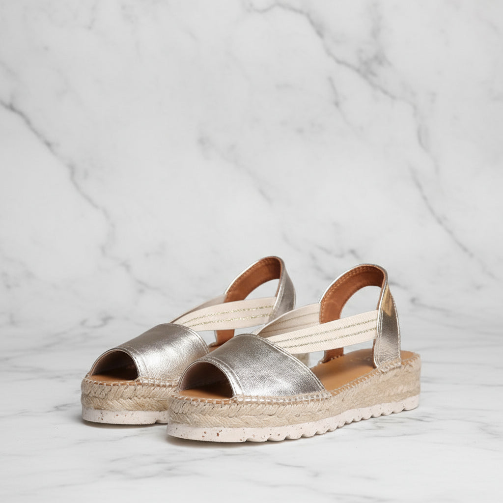 Pair of silver sandals with open toes and jute soles on a light gray background