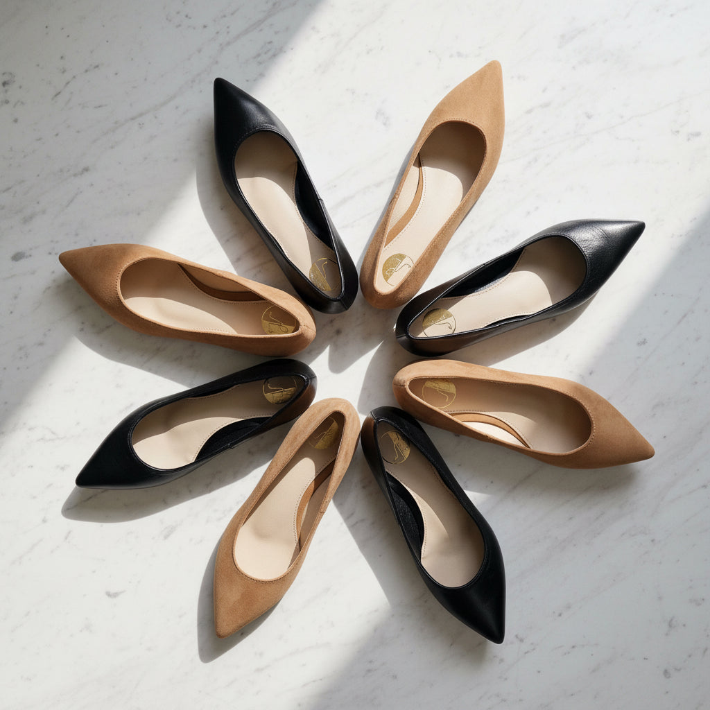 Circle arrangement of black and tan petite pointed-toe flats on marble floor with green leaves