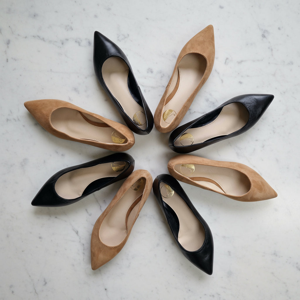 Circle arrangement of black and tan petite pointed-toe flats on marble floor with green leaves
