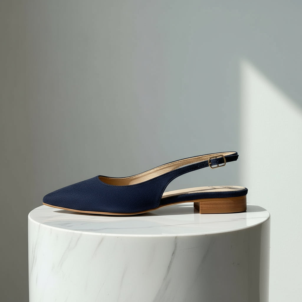 Navy blue slingback shoe on a white marble pedestal against a gray background