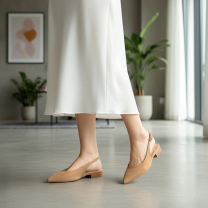 Person wearing beige slingback shoes and white pants in a room with plants and a painting.