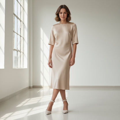 Woman wearing a beige dress standing in a bright room with large windows.