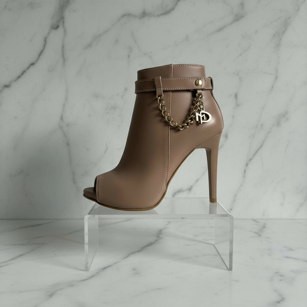Brown high-heeled boot with gold chain and heart charm on a gray background