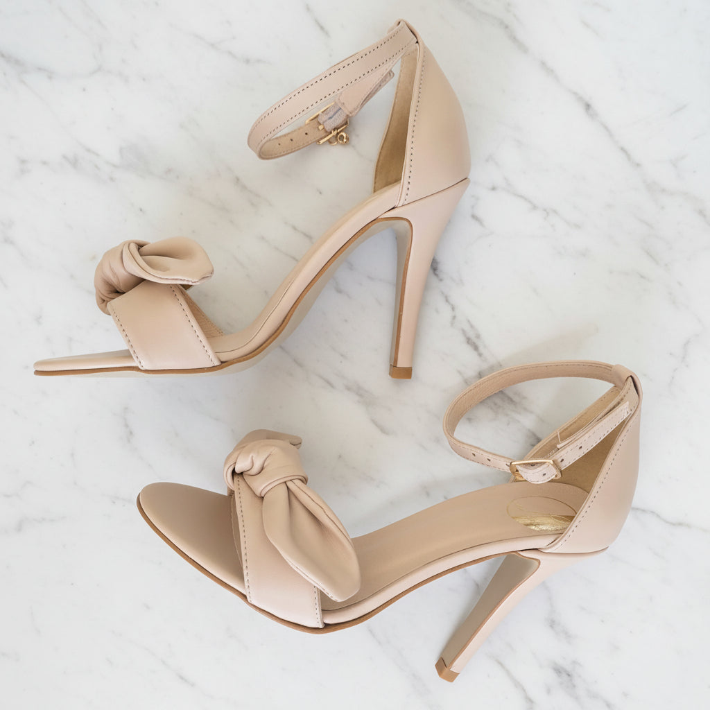 Pair of beige high-heeled sandals with bow details on a gray background