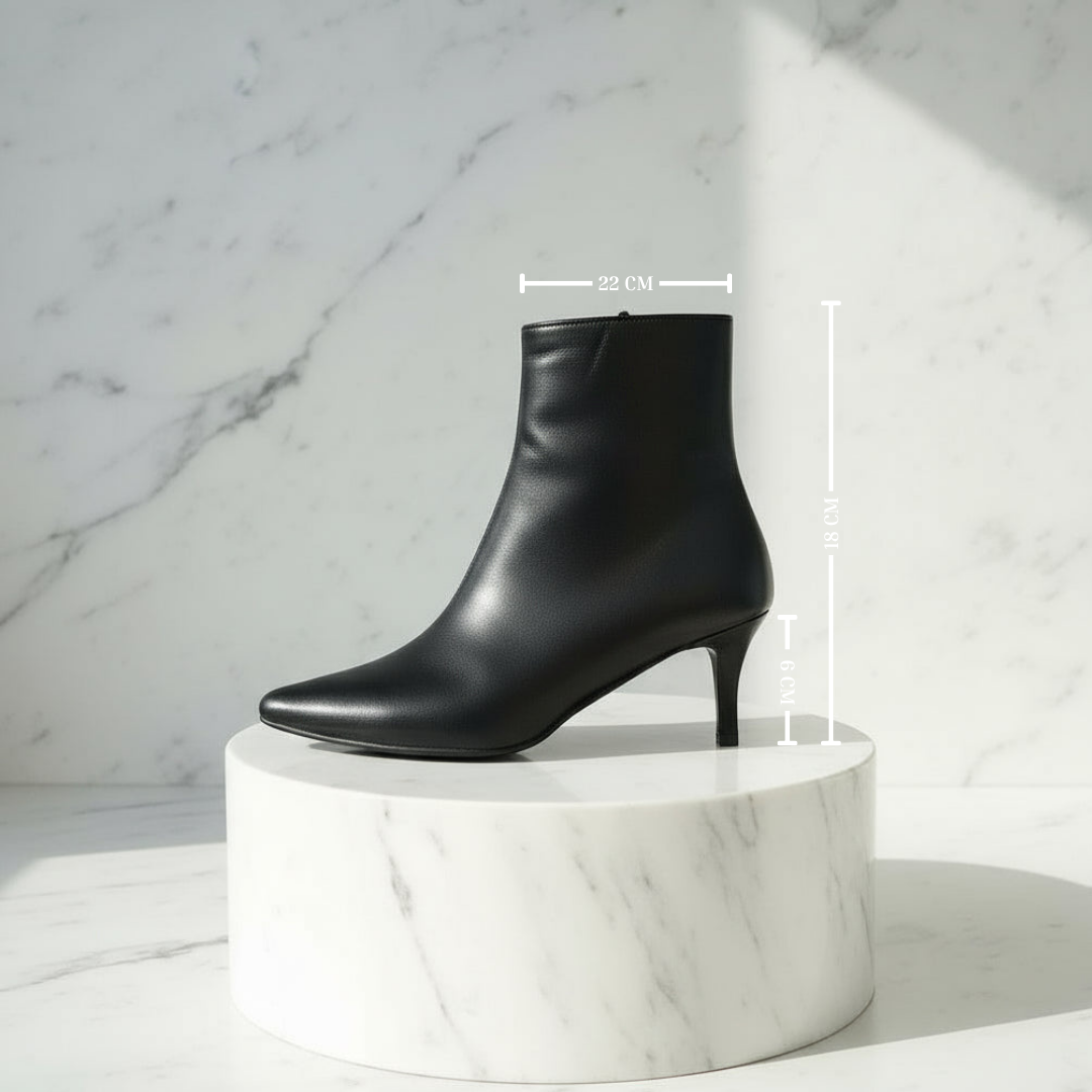 Black high-heeled ankle boot on a marble pedestal with measurement details against a marble background.