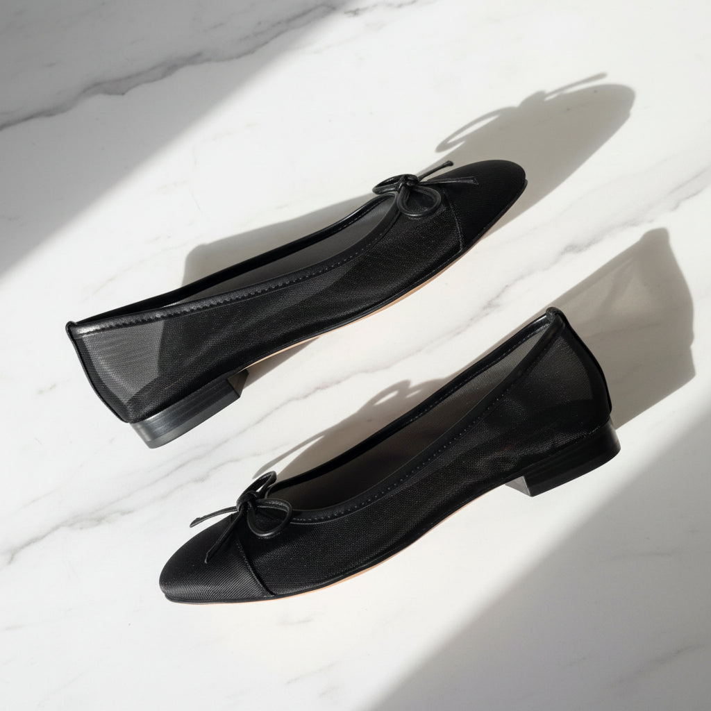Pair of black flat shoes with bow details on a light background