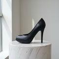 Black high-heeled shoe on a marble pedestal against a light background