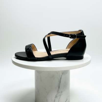 Black leather sandal on a white marble pedestal against a light gray background