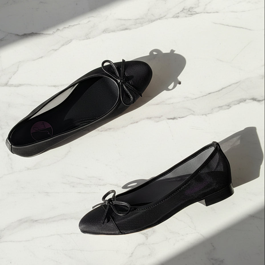 Pair of black flat shoes with a bow on a light background