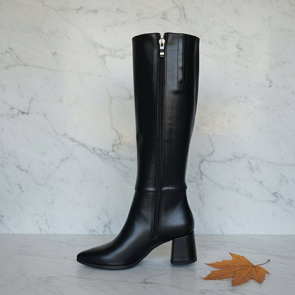 Black knee-high boot with a zipper on a marble surface with a plant in the background