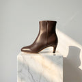 A dark brown leather ankle boot with a low kitten heel, shown from a side profile against a light blue background.