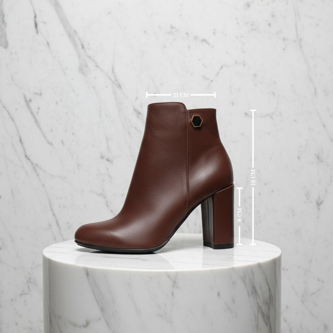 Brown leather ankle boot on a marble pedestal with measurement markings.