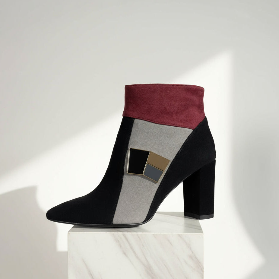 Black, gray, and burgundy ankle boot on a white pedestal with a white background