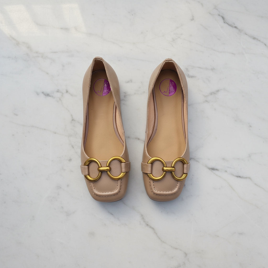 Pair of beige flats with gold buckles on a marble surface