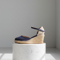 Navy wedge sandal with jute sole on a white marble block against a gray background
