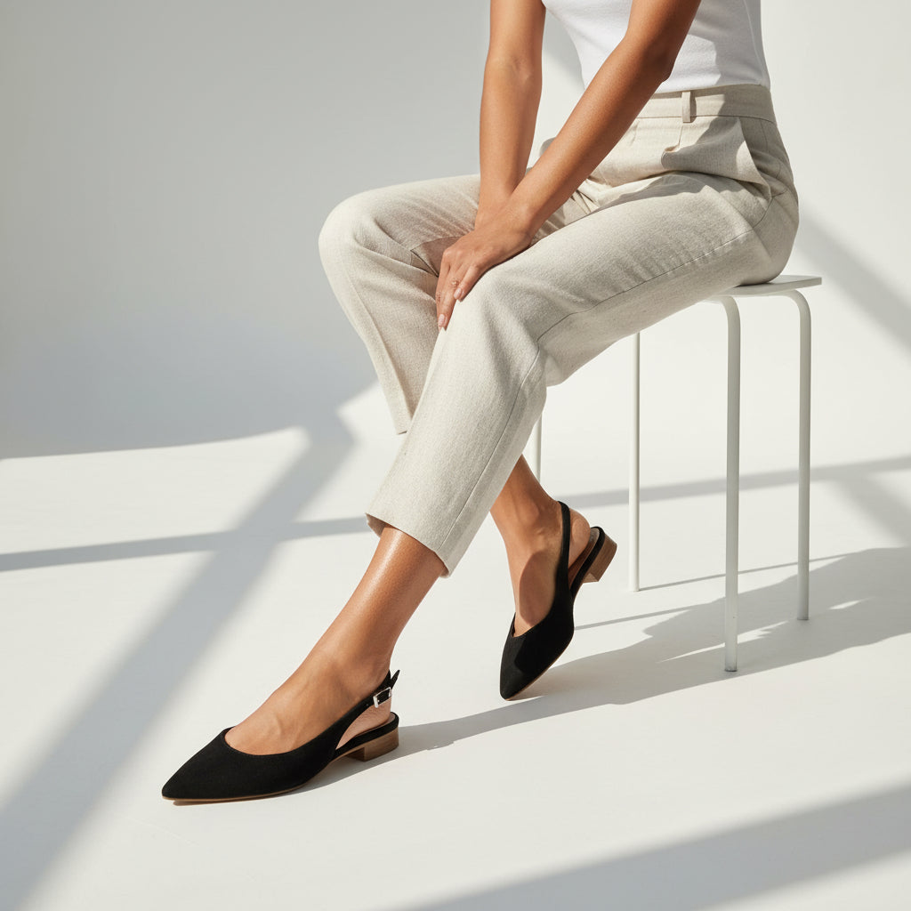 Model sat on a white stool wearing cream linen trousers and contrasting black slingback shoes.