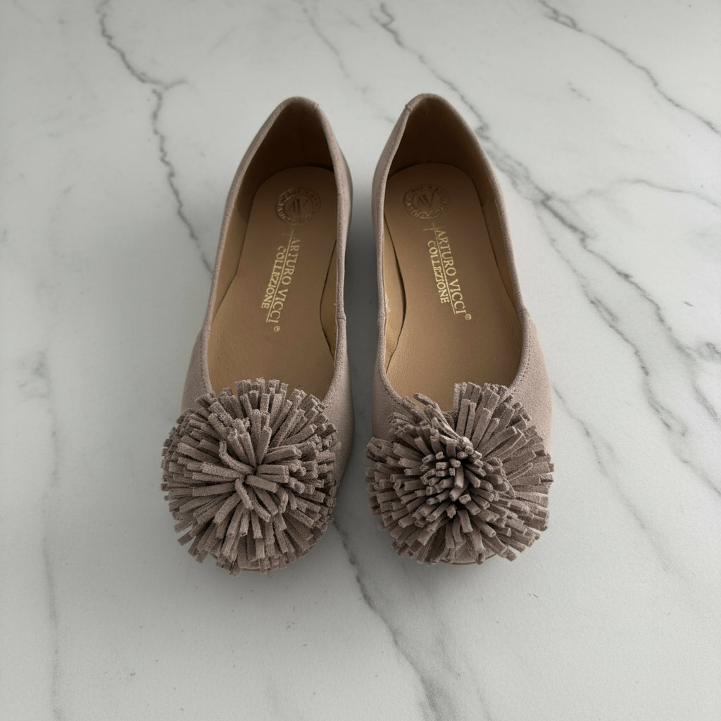 Pair of beige shoes with pom-pom details on a white background