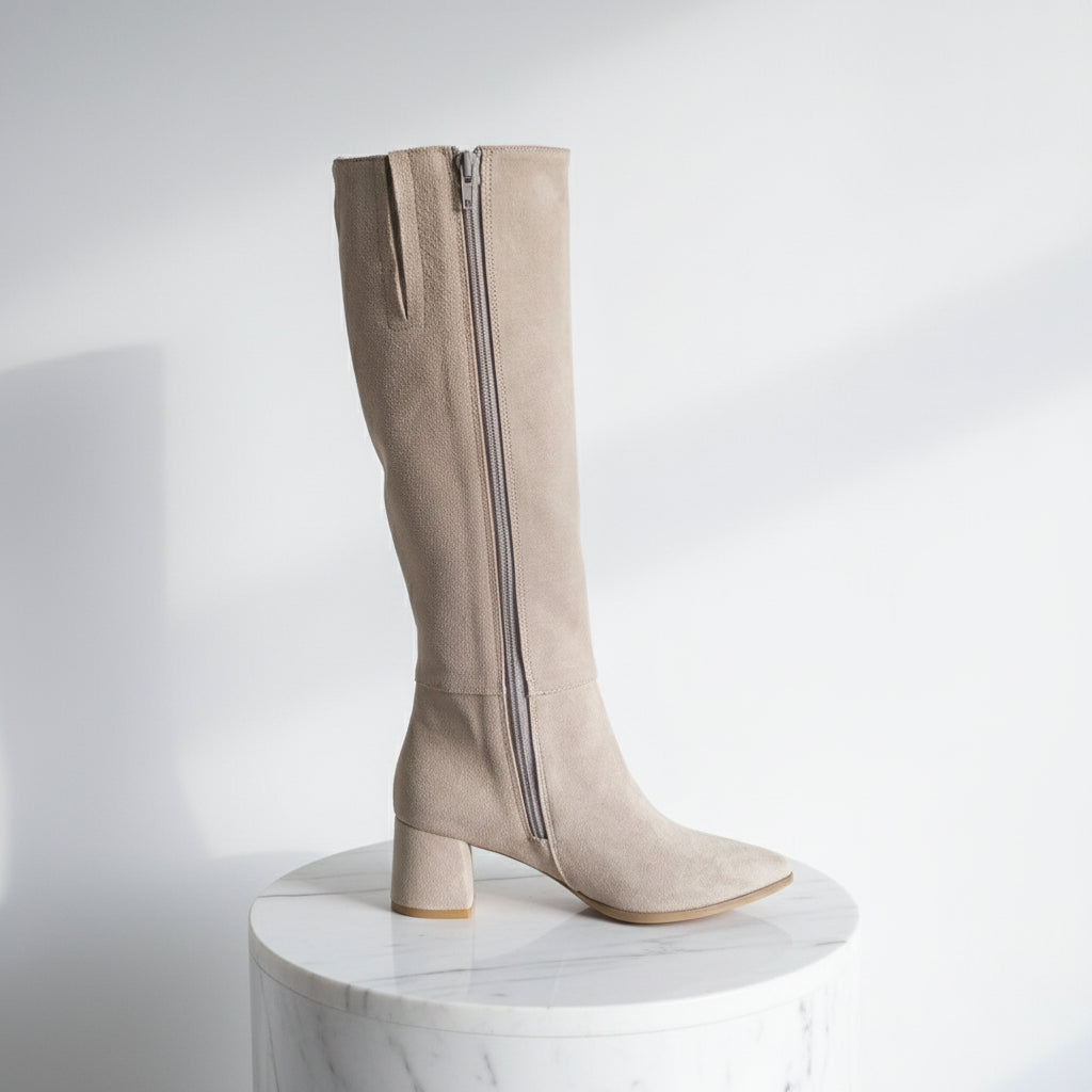 Beige knee-high boot with a zipper on a white surface with a colorful owl toy in the background.
