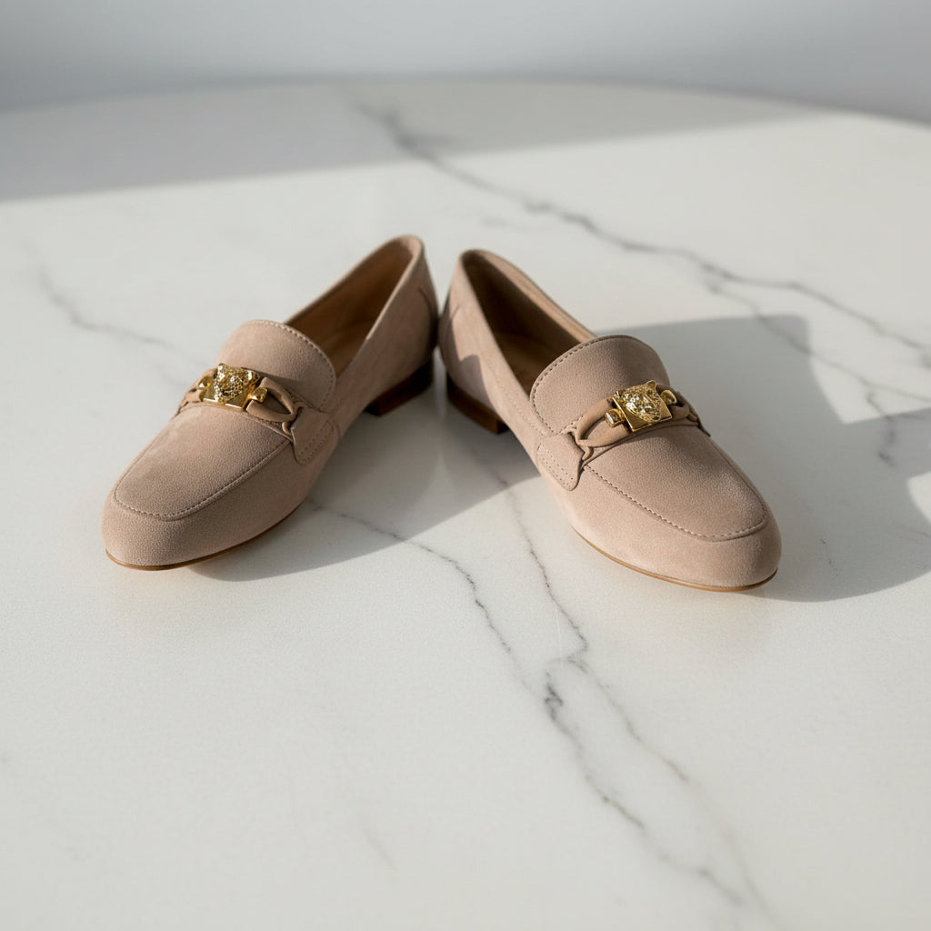 Pair of beige loafers with gold accents on a marble surface