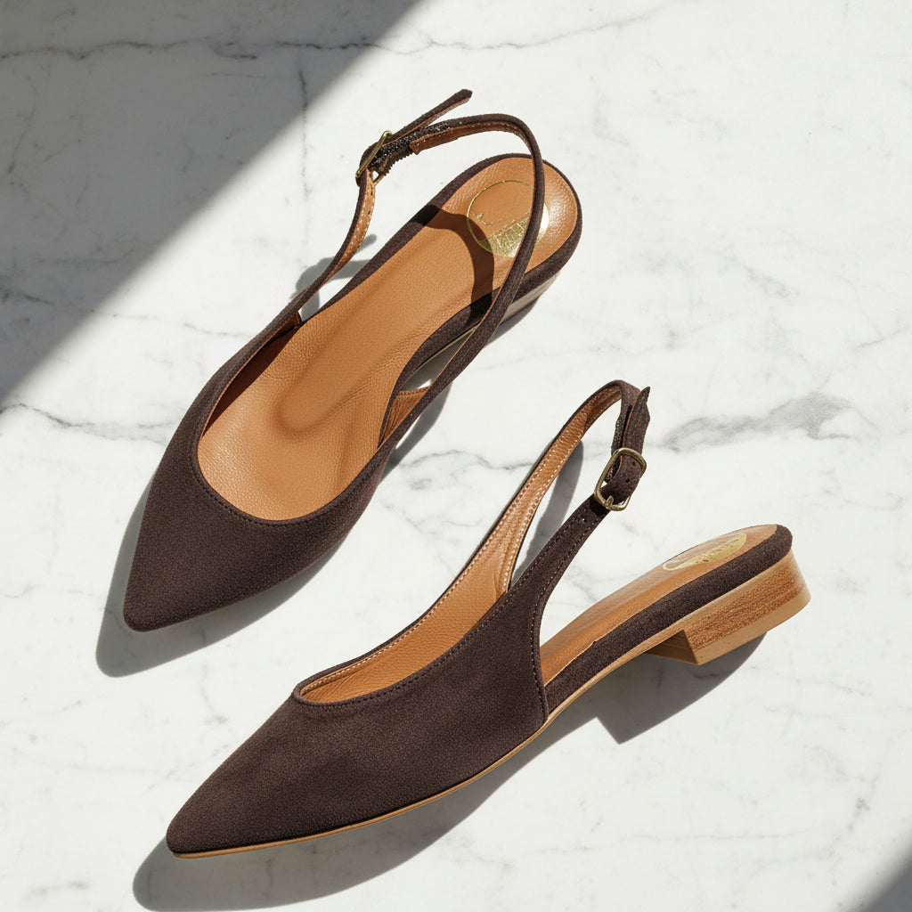 Brown suede slingback flats with a gold buckle and wood inspired heel set on a marble background. 