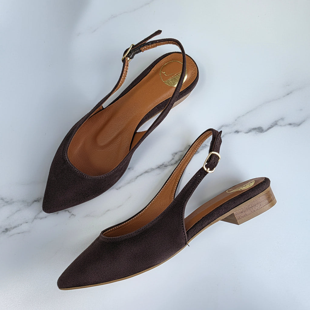 Brown suede slingback flats with a gold buckle and wood inspired heel set on a marble background. 