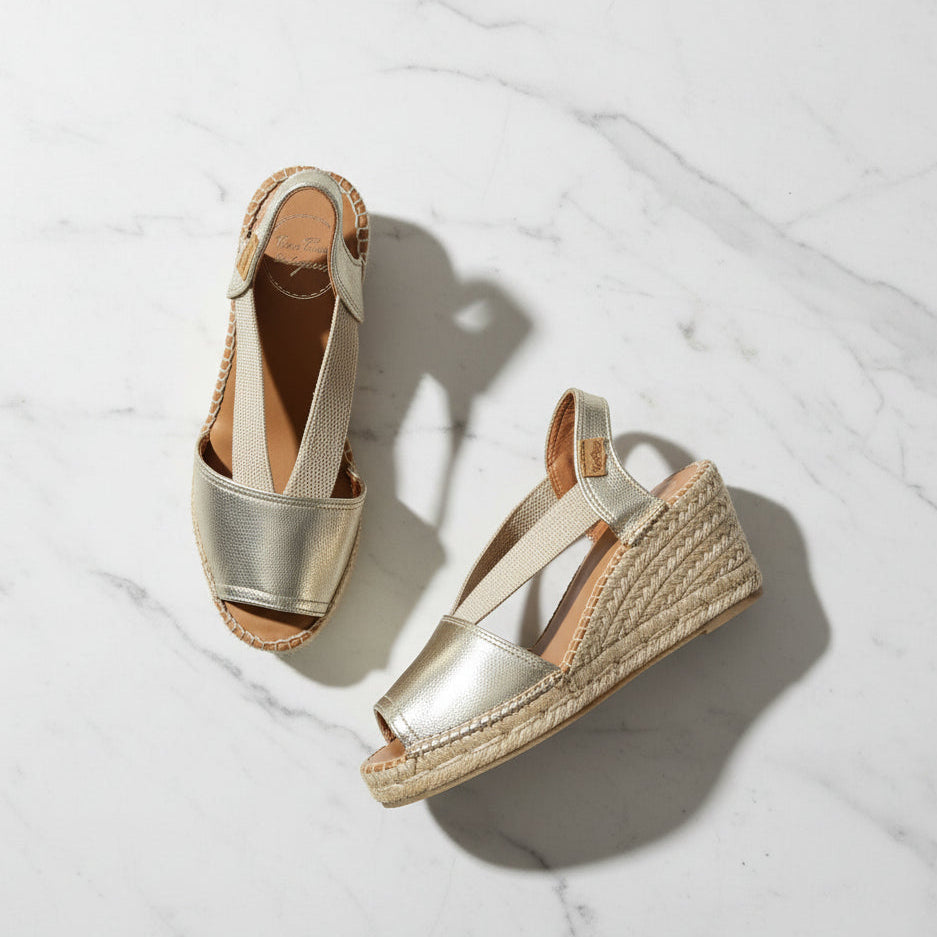 Pair of gold wedge sandals with espadrille soles on a light marble background