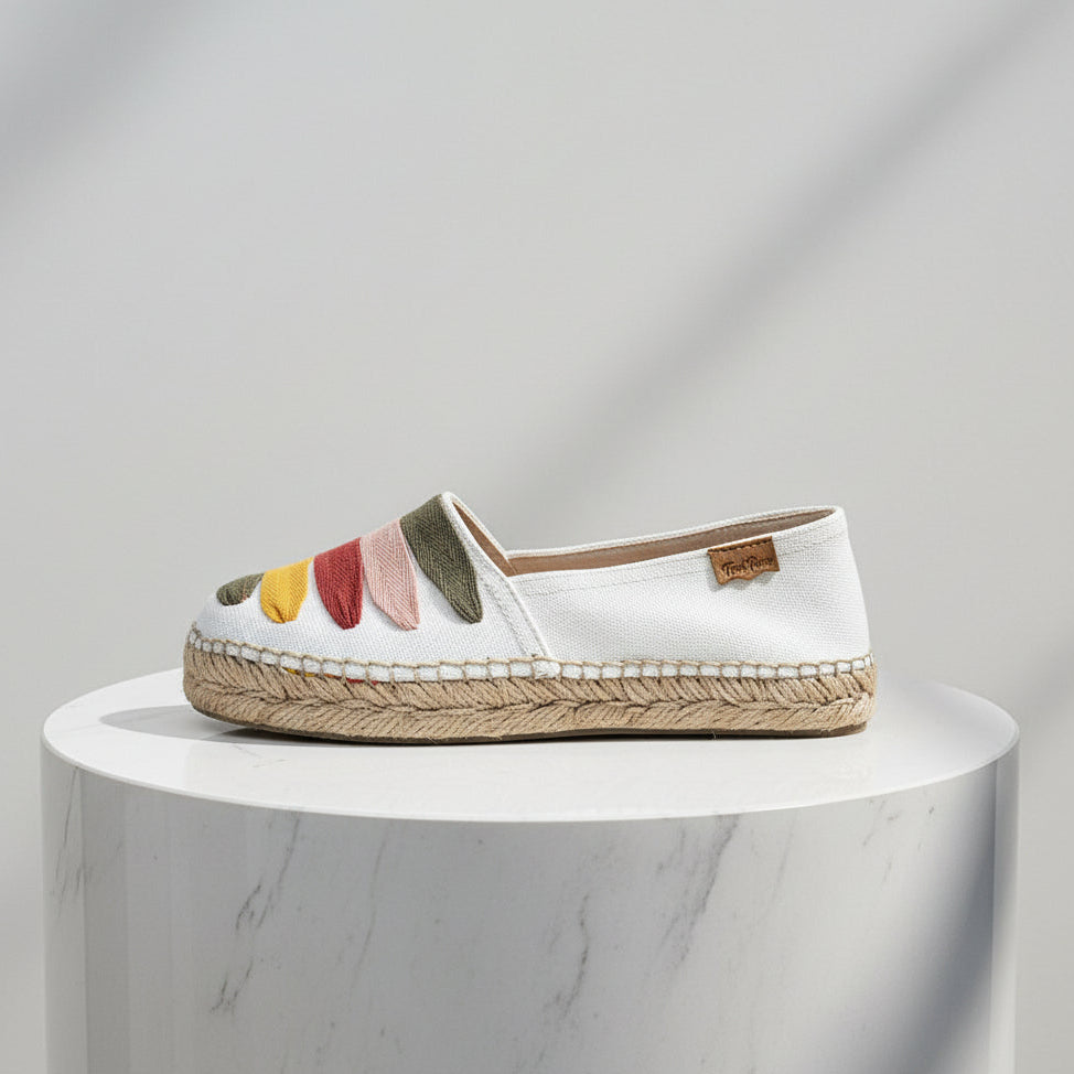 White espadrille shoe with colorful accents on a white pedestal against a gray background