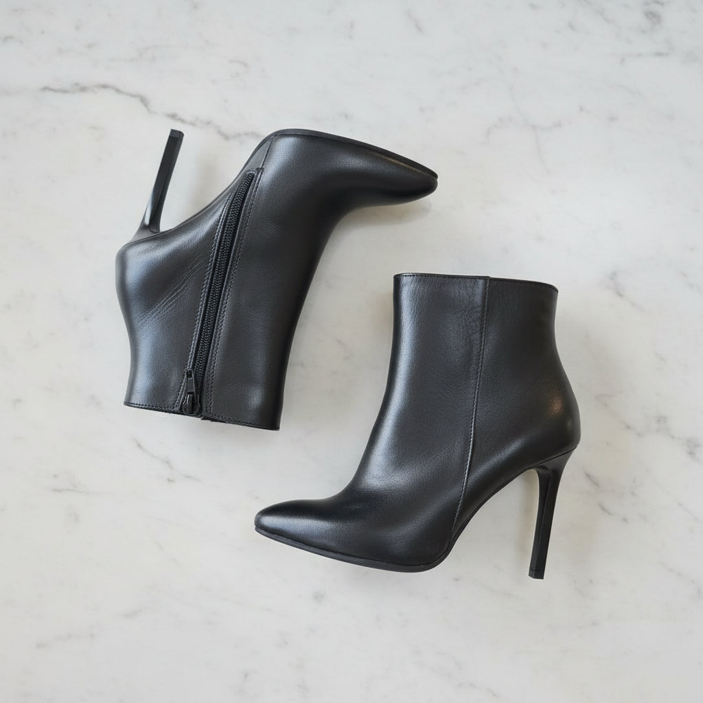 Black high-heeled ankle boots on a light marble background