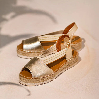 A pair of gold leather espadrille sandals with elasticated side straps and a jute wedge heel on a light background.
