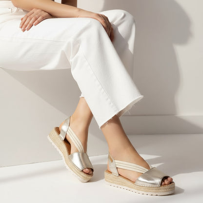 Gold leather sandals worn with white  pants on a white background