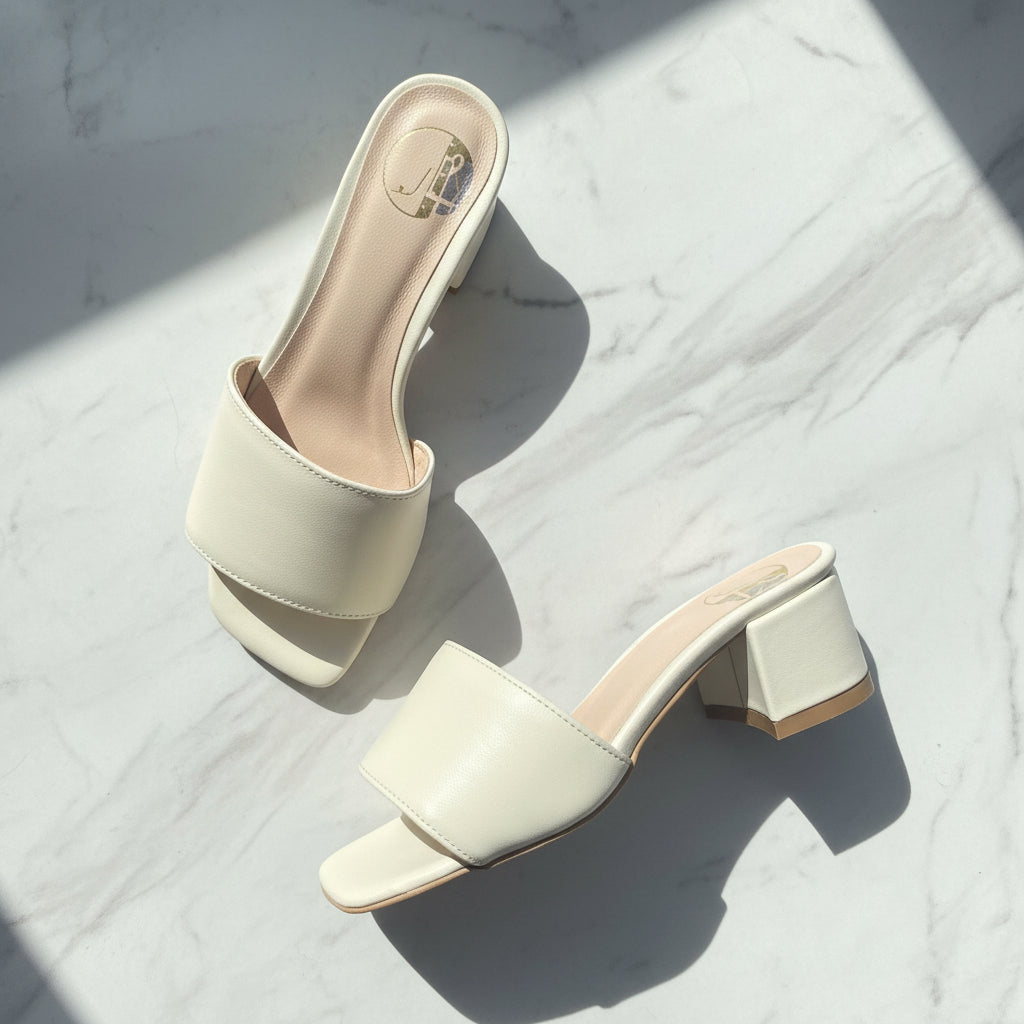 Pair of white high-heeled sandals on a light marble surface