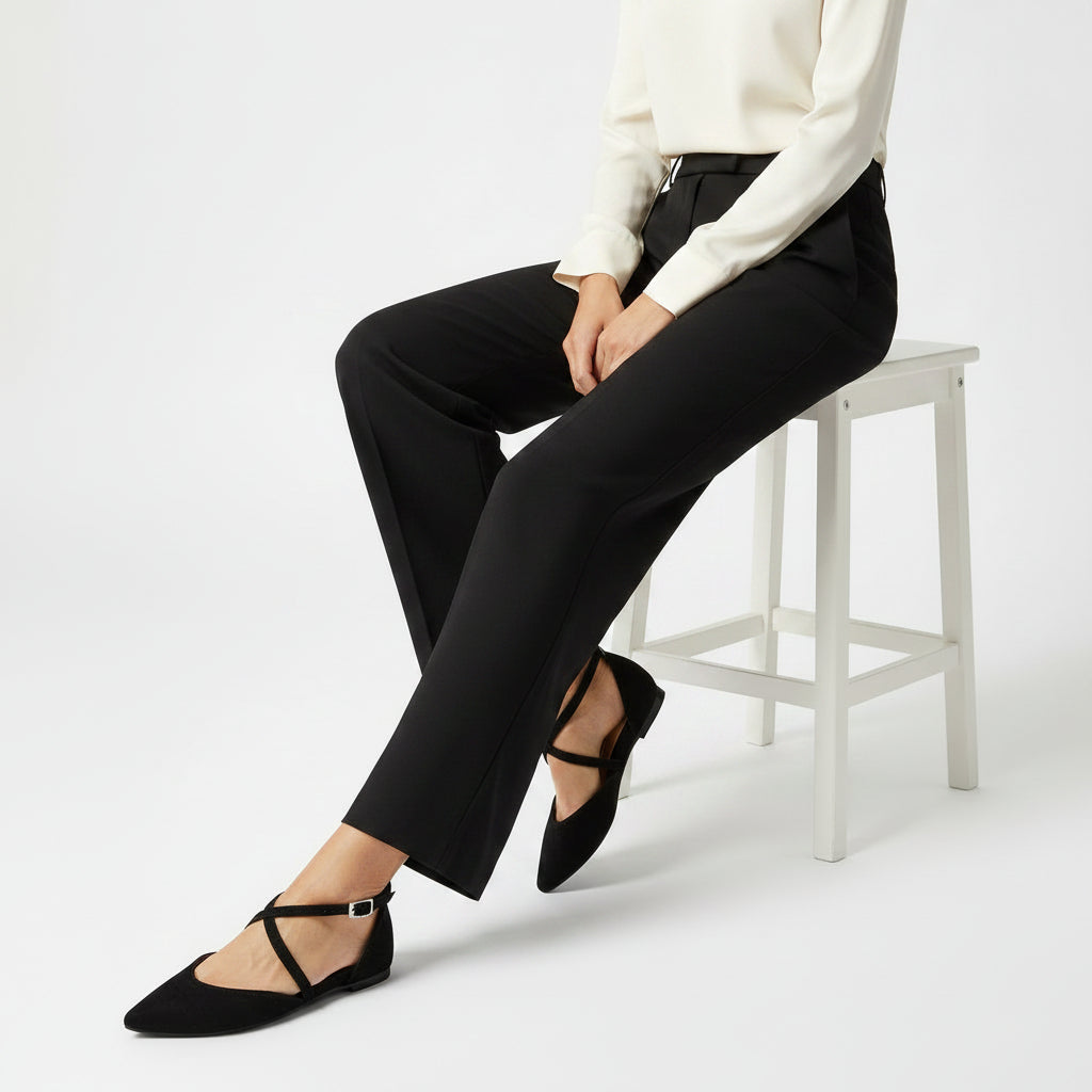 Person wearing black pants and black flats sitting on a white stool against a white background