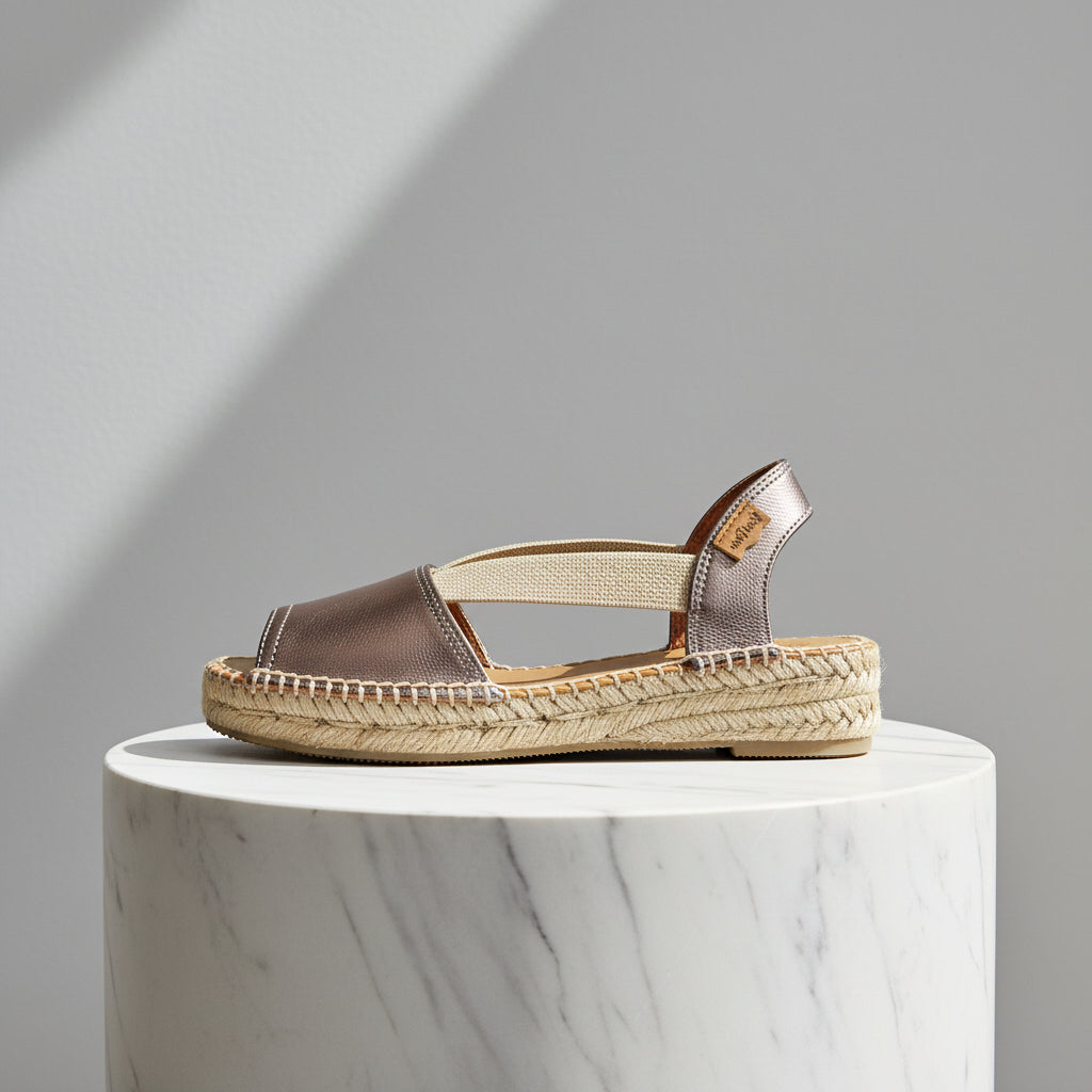 Metallic leather sandal with woven sole on a marble pedestal against a grey background