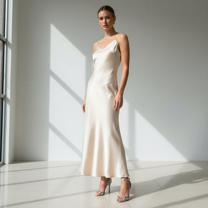 Silver high heel sandals worn on feet with ankle straps, crossed legs background plant.