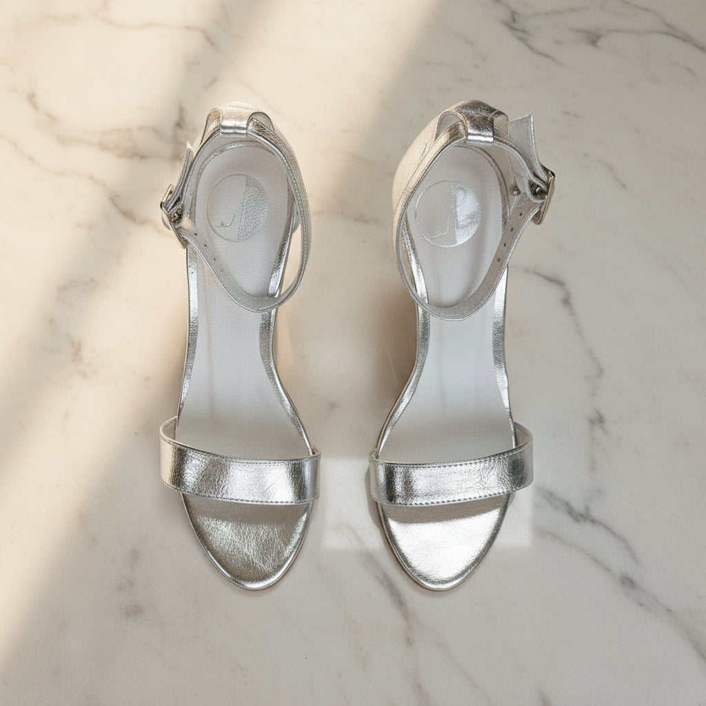 Front view of pair of silver high heel sandals with ankle straps on marble.