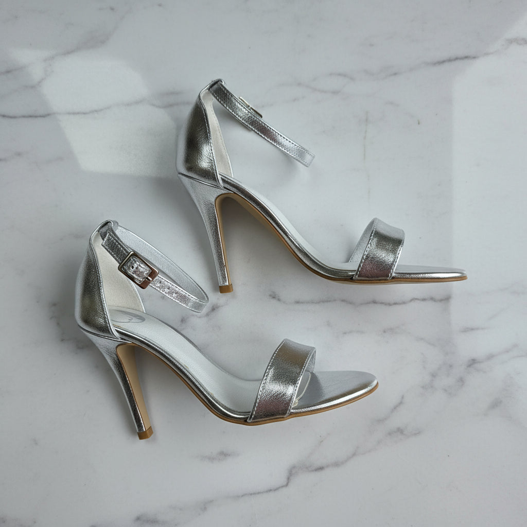 Side profile flat lay of silver high heel sandals with ankle straps.