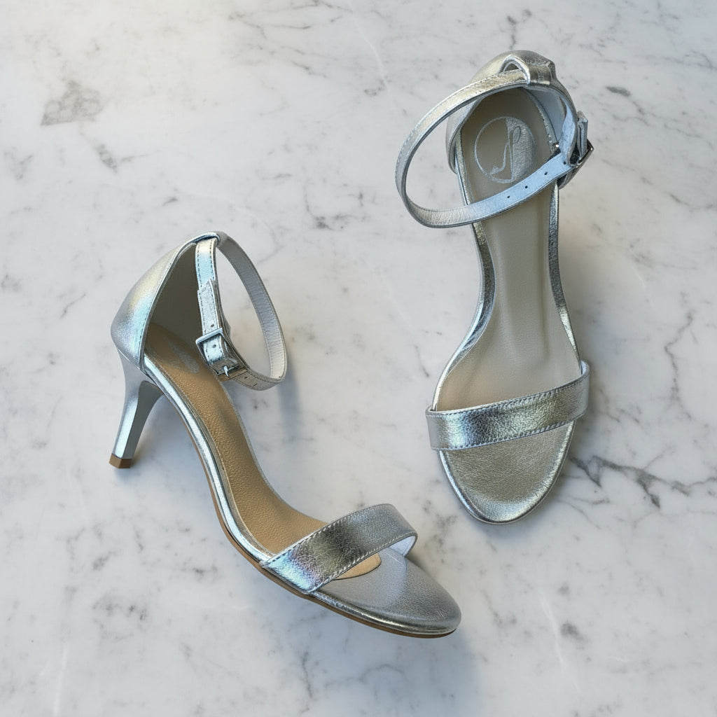 Petite ankle strap kitten heels in silver leather set on a marble table.