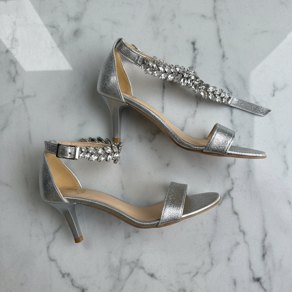 Silver high-heeled sandals with rhinestone straps on a marble surface