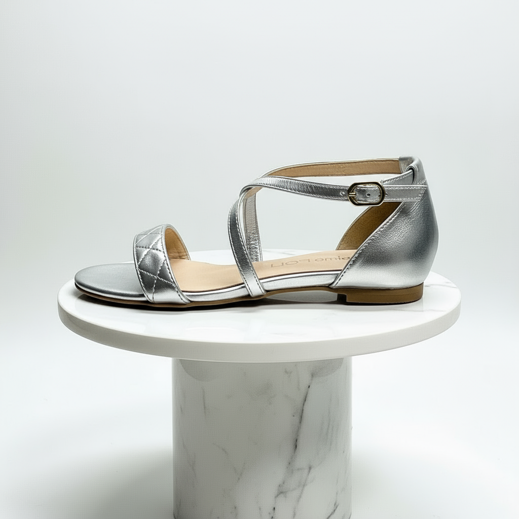 Silver leather sandal on a white marble pedestal against a light gray background