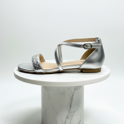 Silver leather sandal on a white marble pedestal against a light gray background